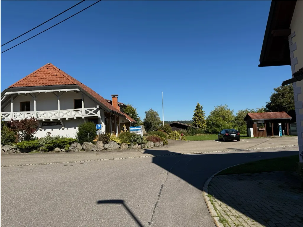 Weißes Gebäude mit rotem Ziegeldach und Schriftzug „Bürgerhaus“ an einer Dorfstraße mit Parkplatz und Auto.