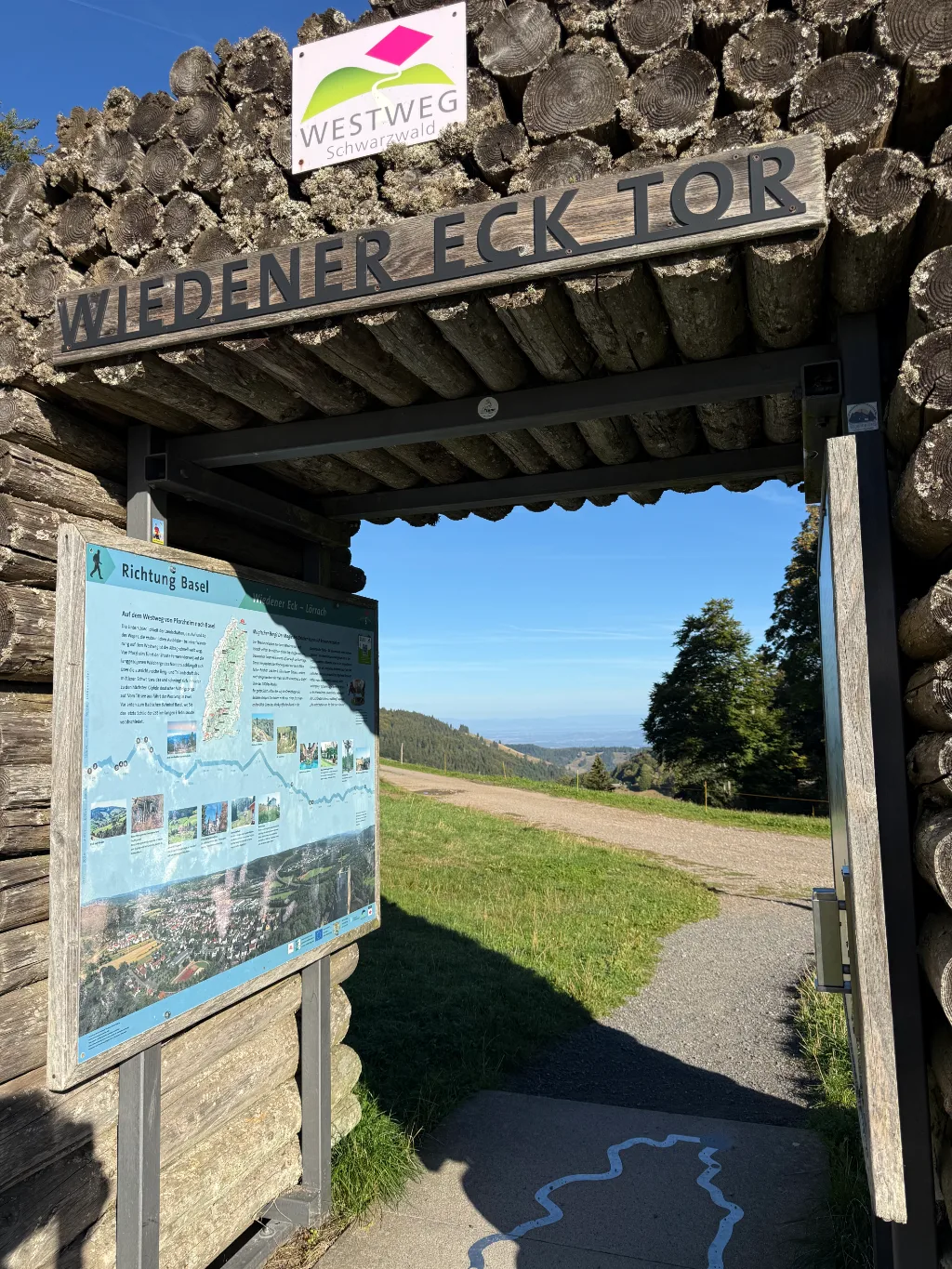 Holztor „Wiedener Eck Tor“ mit Westweg-Schild und Infotafel „Richtung Basel“, Blick auf Wiese und Wanderweg.