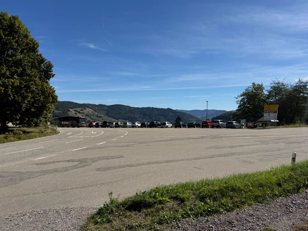 Gefüllter Parkplatz am Wiedener Eck mit Reisebus und Autos vor bewaldeten Schwarzwaldhöhen bei blauem Himmel