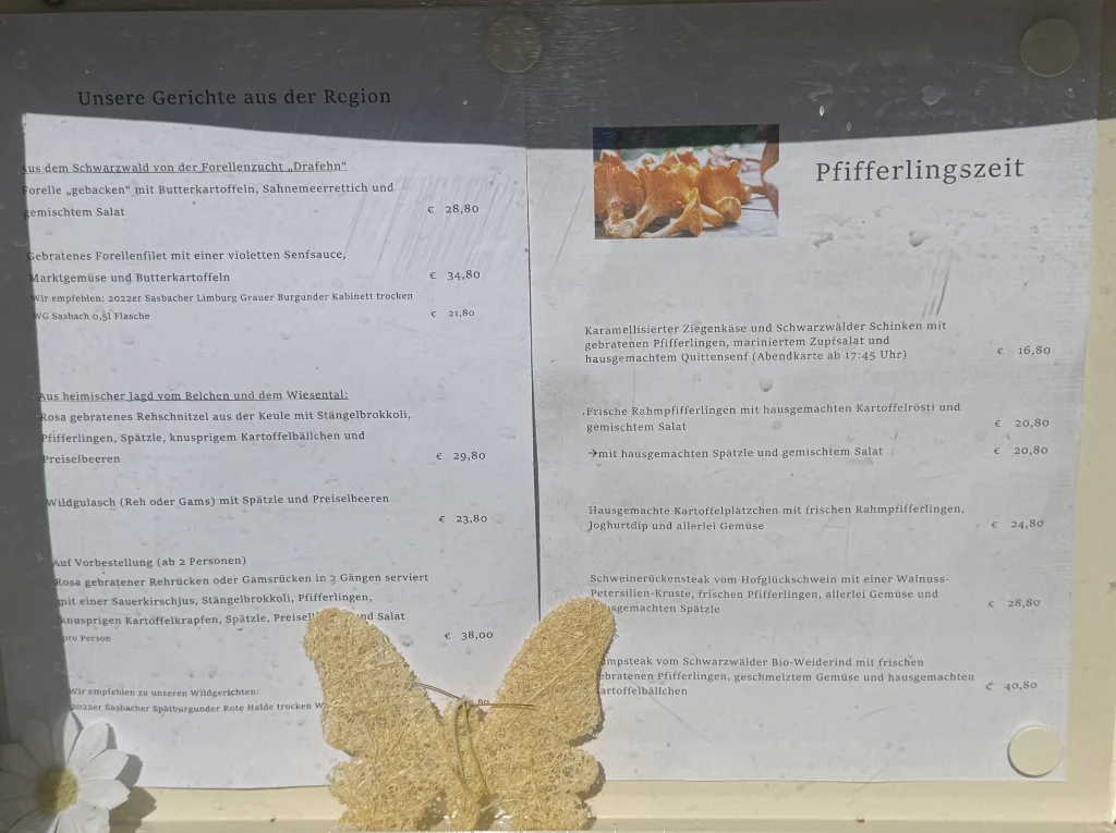 Aushang der Speisekarte mit regionalen Gerichten und Pfifferlingsgerichten im Schaukasten, davor eine Deko-Schmetterling.